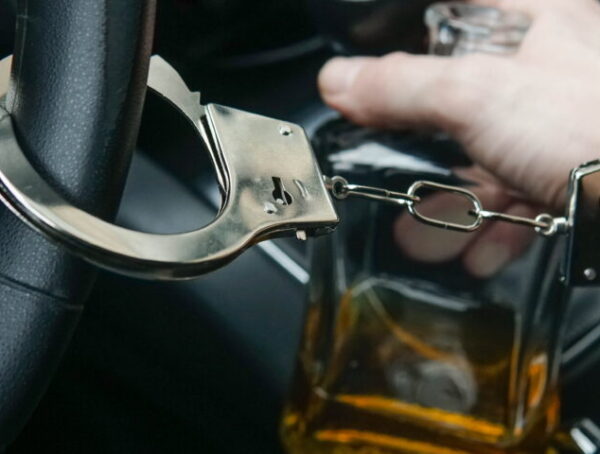 Man in handcuffs holding an alcohol bottle inside a car representing DUI arrest and DUI bail bonds San Diego process
