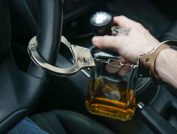Man in handcuffs holding an alcohol bottle inside a car representing DUI arrest and DUI bail bonds San Diego process