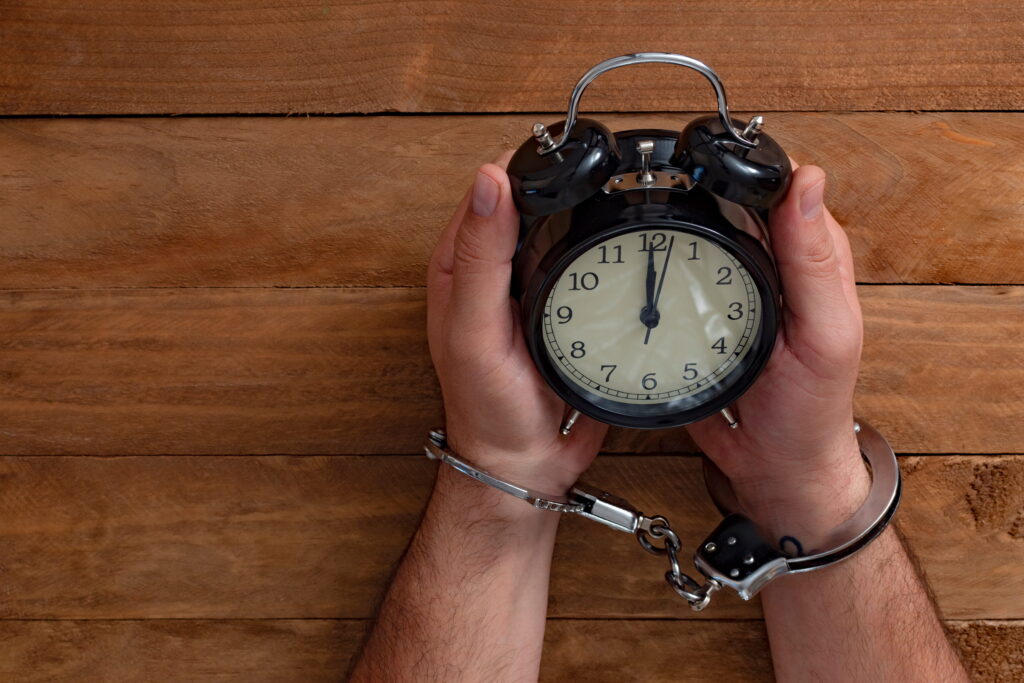 Handcuffed individual sitting under a clock symbolizing urgency after arrest and the importance of National City bail bonds in early legal action