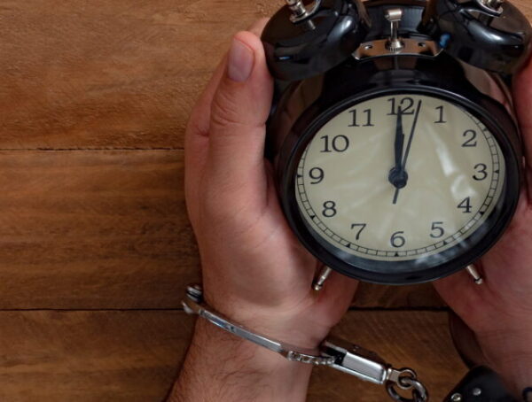 Handcuffed individual sitting under a clock symbolizing urgency after arrest and the importance of National City bail bonds in early legal action