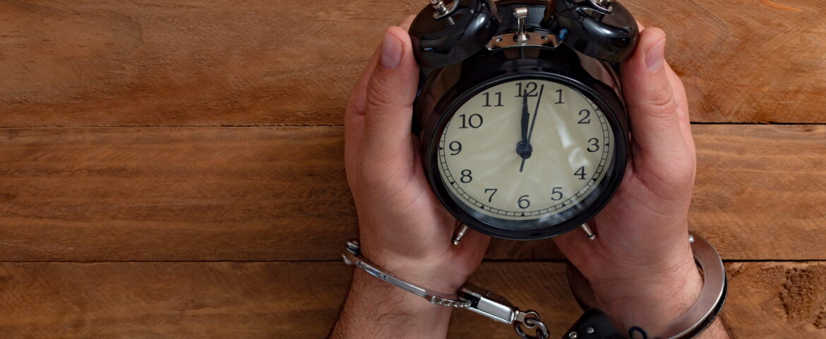 Handcuffed individual sitting under a clock symbolizing urgency after arrest and the importance of National City bail bonds in early legal action