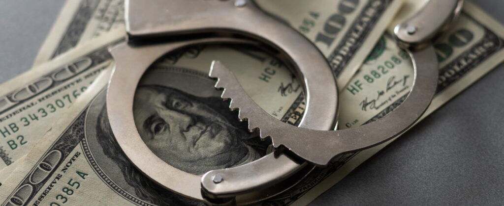 Handcuffs placed over hundred-dollars representing bail and financial considerations in Downtown San Diego bail bonds situations